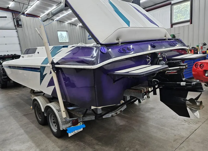 Slide: The Image of 2000 Eliminator 25 Daytona boat in garage, purple and white design, on trailer. - 4