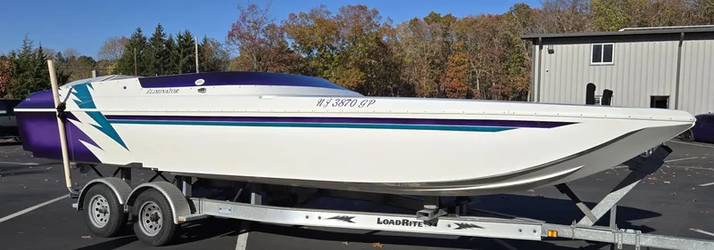 Slide: The Image of 2000 Eliminator 25 Daytona boat on trailer, white with blue and purple accents, parked outdoors. - 8