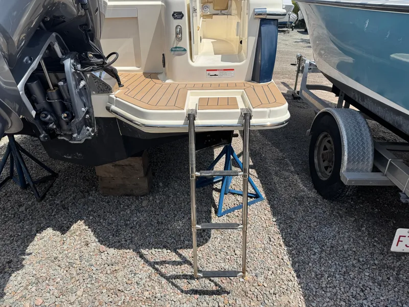 Slide: The Image of 2019 Scout 235 XSF boat with swim platform and ladder, parked on gravel. - 9