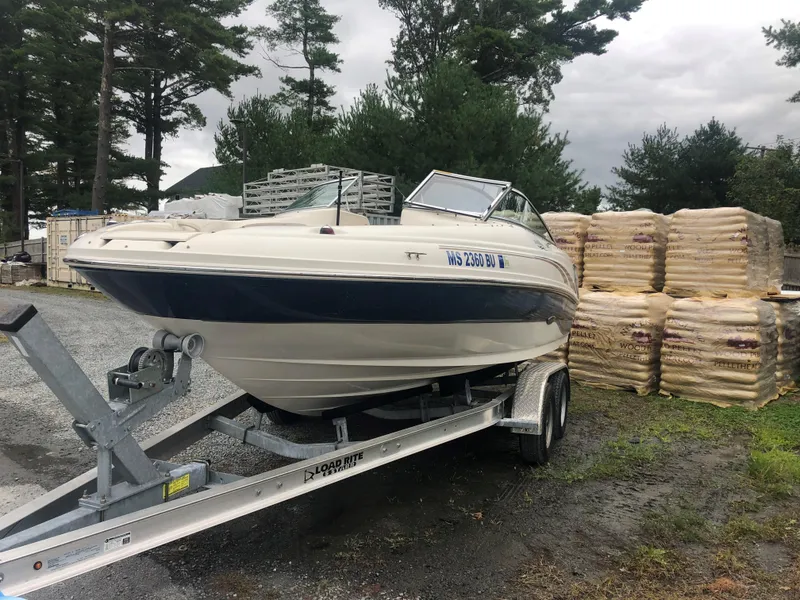 Slide: The Image of 2003 Sea Ray 200 Sundeck boat on trailer, parked outdoors near stacked materials. - 2