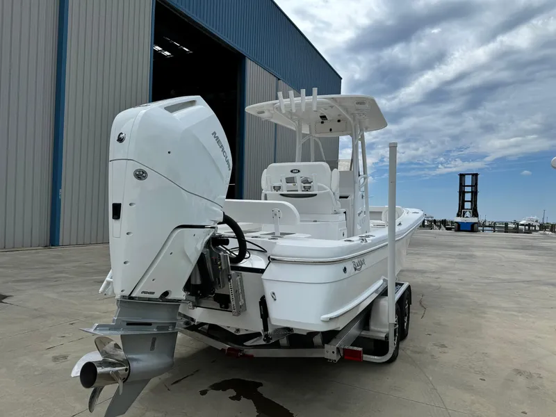 Slide: The Image of 2025 BlackJack 256 Coastal boat with powerful outboard motor, parked near a large warehouse. - 4