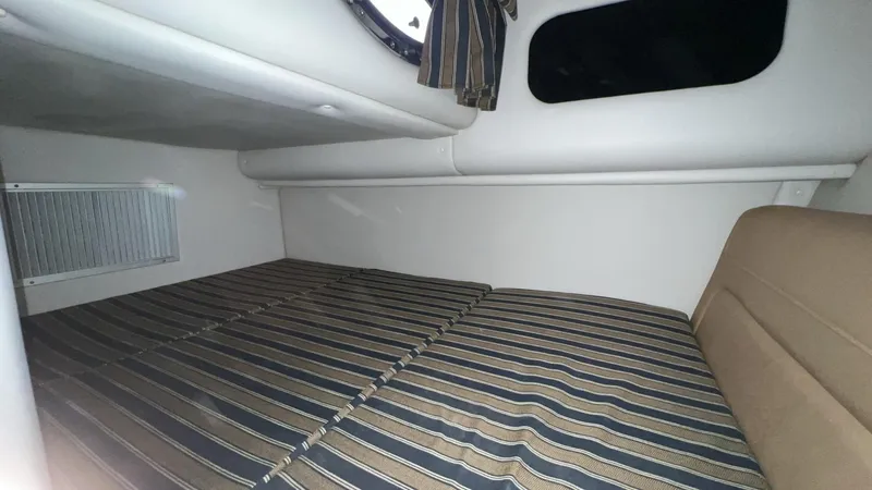 Slide: The Image of 2014 Crownline 294 CR cabin interior with striped bedding and window. - 23