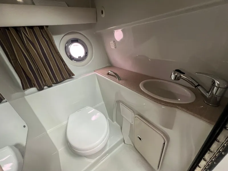 Slide: The Image of 2014 Crownline 294 CR boat bathroom with sink, toilet, and porthole window. - 25