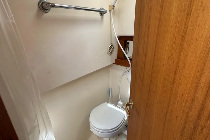 Slide: The Image of 2002 Mainship Pilot 34 boat bathroom with toilet, shower, and wooden door. - 12