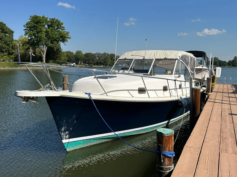 Slide: The Image of 2002 Mainship Pilot 34 docked on a sunny day, surrounded by calm water and trees. - 2