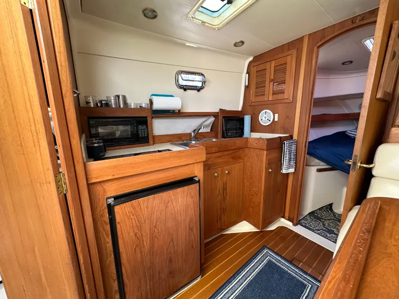 Slide: The Image of 2002 Mainship Pilot 34 interior with wood cabinetry, kitchenette, and cozy sleeping area. - 7