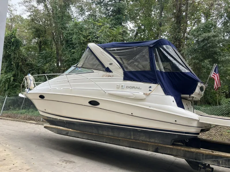 The Image of 2001 Doral 270 SC boat with blue canopy on trailer, American flag in background. - 0