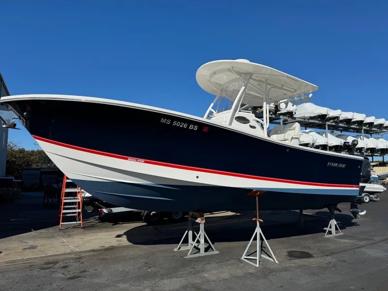 Slide: The Image of 2017 Regulator 25 CC boat on stands, blue hull, white top, sunny day. - 1