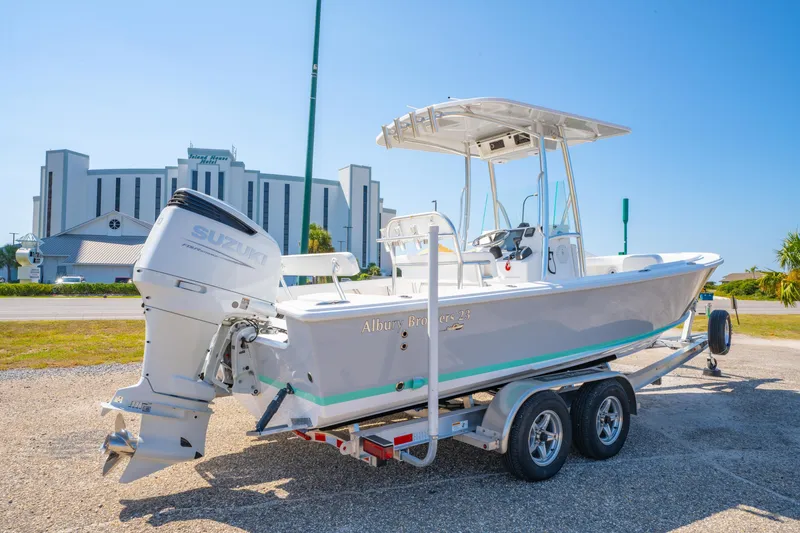 Slide: The Image of 2026 Albury Brothers 23 boat on trailer with Suzuki engine, parked near a modern building. - 6