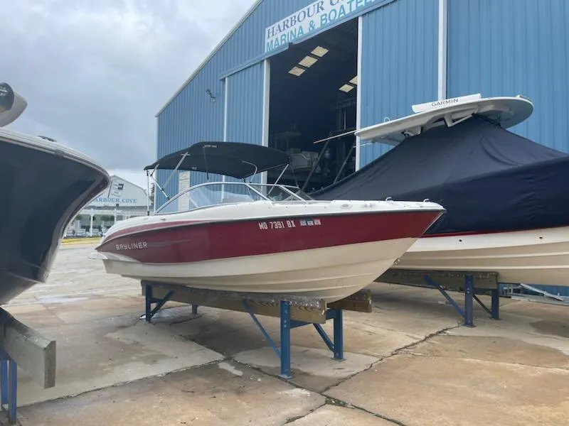 The Image of 2011 Bayliner 235 Bowrider boat on stands outside a marina building. - 0