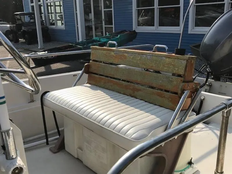 Slide: The Image of 1988 Boston Whaler 170 Montauk boat interior with white cushioned seating and wooden backrest. - 4