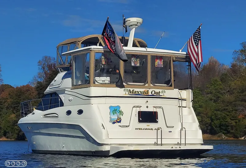 Slide: The Image of 2000 Sea Ray 380 Aft Cabin yacht on water, flags flying, forested background. - 29