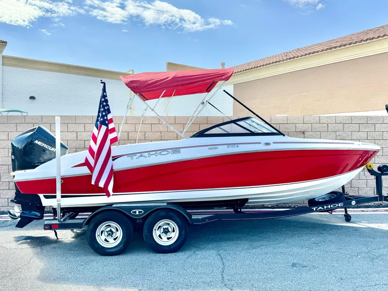 Slide: The Image of Red 2022 Tahoe 210 S boat with American flag and trailer, parked outdoors. - 0