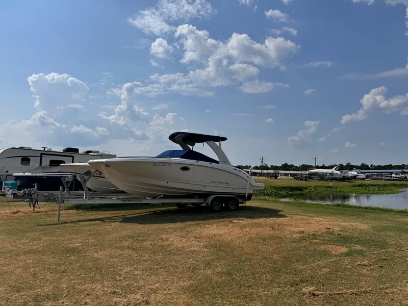 The Image of 2012 Chaparral 264 Sunesta boat on trailer, parked near RVs by a lake. - 0