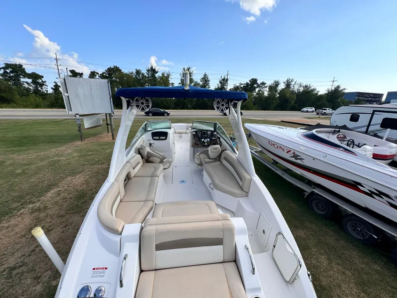 Slide: The Image of 2012 Chaparral 264 Sunesta boat with spacious seating and canopy, parked on grass. - 2