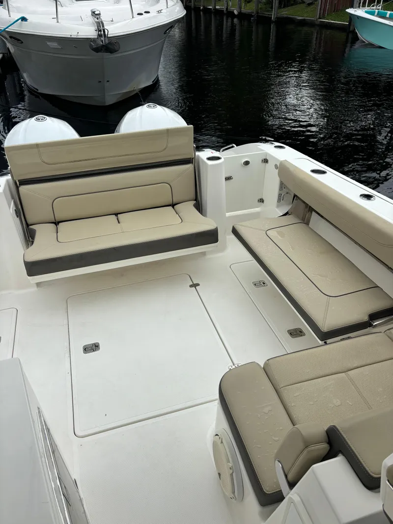 Slide: The Image of 2020 Pursuit 325 Dual Console boat interior with beige seating, docked by the water. - 10