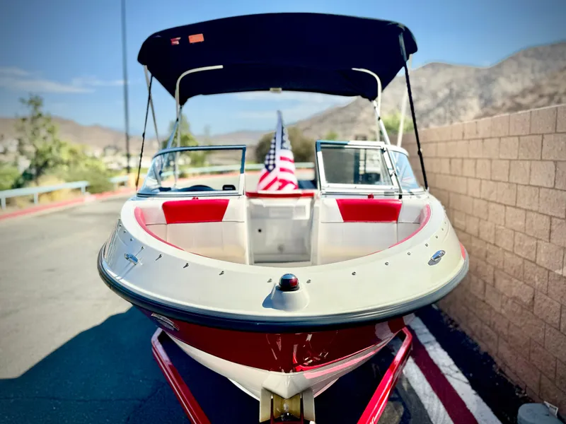 Slide: The Image of 2013 Bayliner 185 Bowrider with canopy, parked on a trailer, American flag displayed. - 3