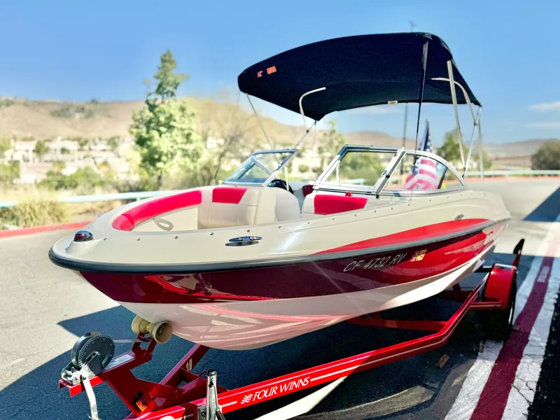 Slide: The Image of 2013 Bayliner 185 Bowrider boat with red accents on a trailer, parked outdoors. - 4