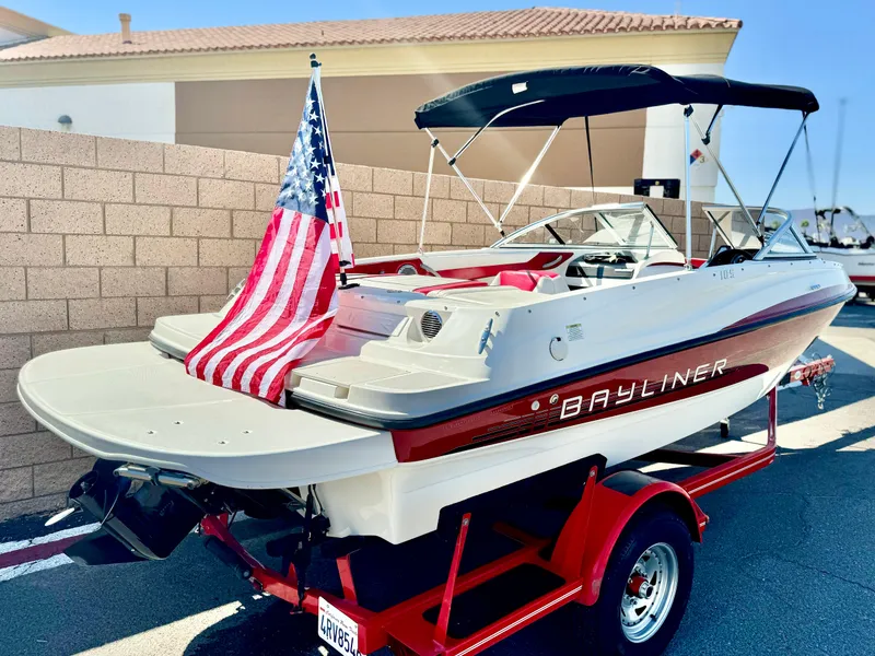 Slide: The Image of 2013 Bayliner 185 Bowrider on trailer with American flag, parked outdoors. - 6