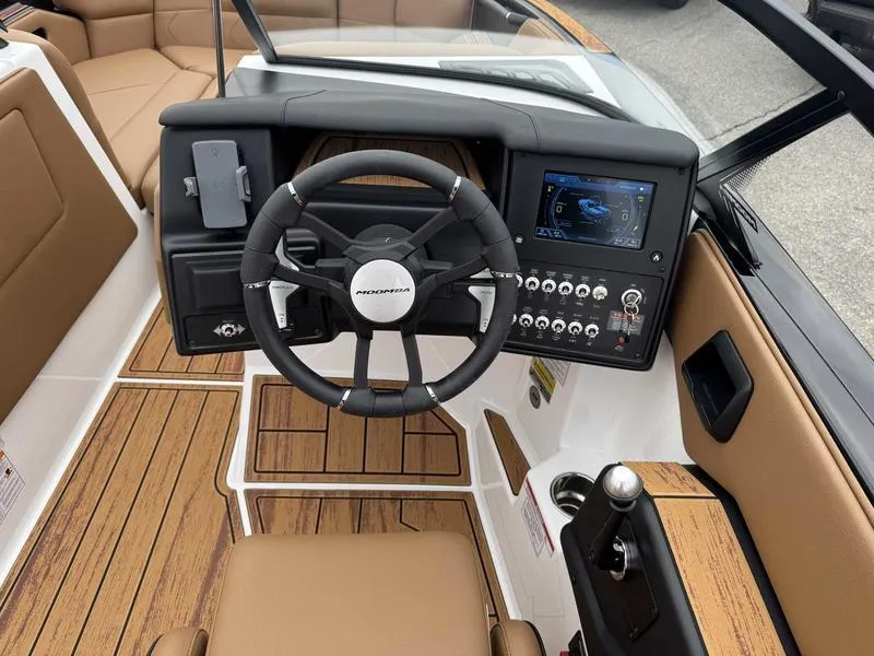 Slide: The Image of 2025 Moomba Tykon boat interior with steering wheel, control panel, and brown seating. - 12