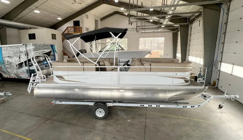 Slide: The Image of 2023 Starcraft LX 22 R pontoon boat in a spacious indoor showroom. - 0