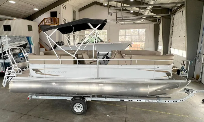 Slide: The Image of 2023 Starcraft LX 22 R pontoon boat in a showroom, featuring beige seating and a black canopy. - 1