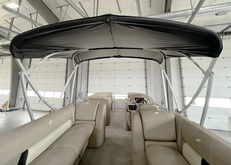 Slide: The Image of 2023 Starcraft LX 22 R pontoon boat interior with canopy in a warehouse setting. - 23