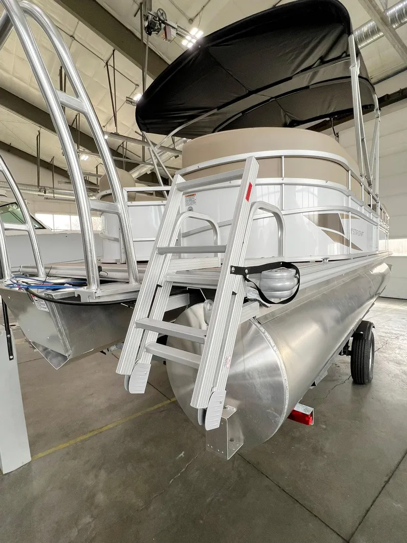 Slide: The Image of 2023 Starcraft LX 22 R pontoon boat in a showroom, featuring a sleek aluminum design. - 27