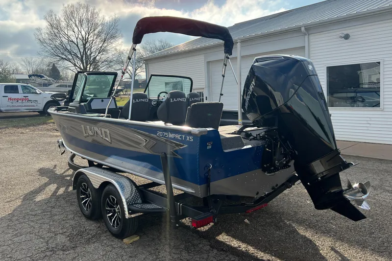 Slide: The Image of 2025 Lund 2075 IMPACT XS boat with outboard motor on trailer, parked outdoors. - 7