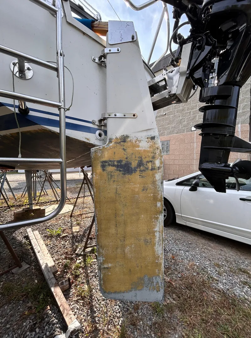 Slide: The Image of 1986 CAL 22 sailboat rudder with visible wear, parked near a white car. - 20