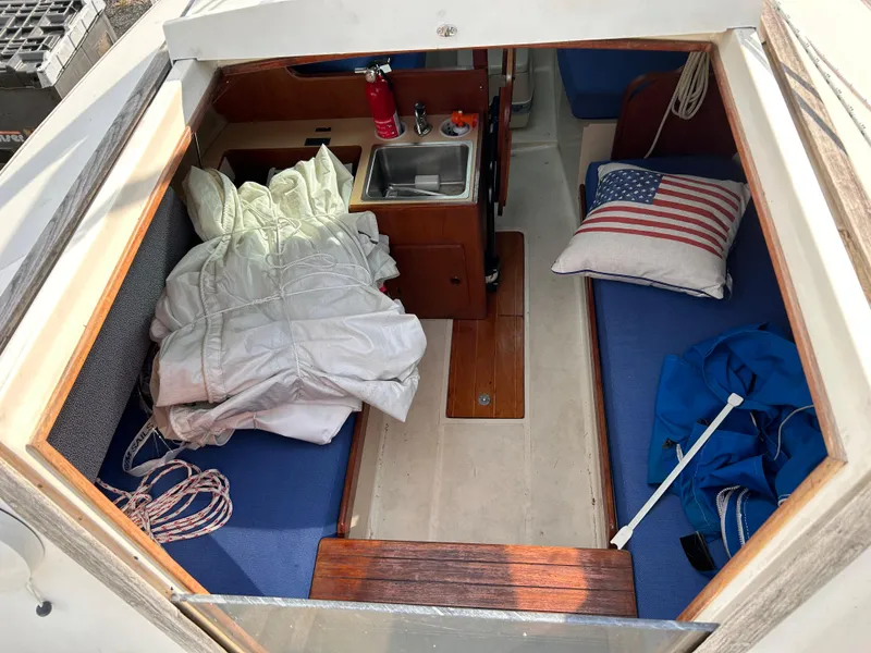 Slide: The Image of Interior of 1986 CAL 22 sailboat with cozy seating, sink, and American flag pillow. - 25