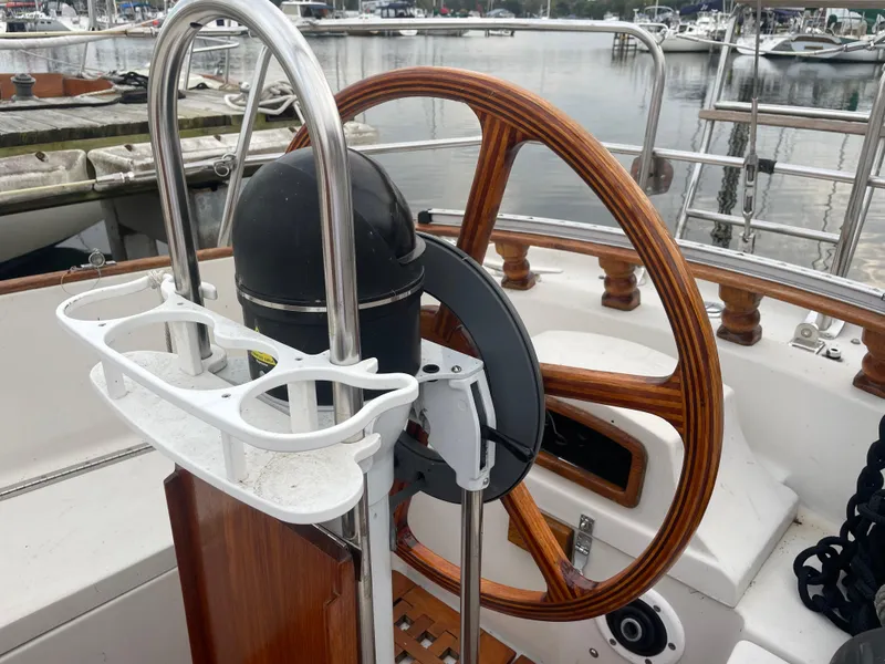 Slide: The Image of 1985 Bayfield 32 sailboat helm with wooden wheel and marina background. - 11