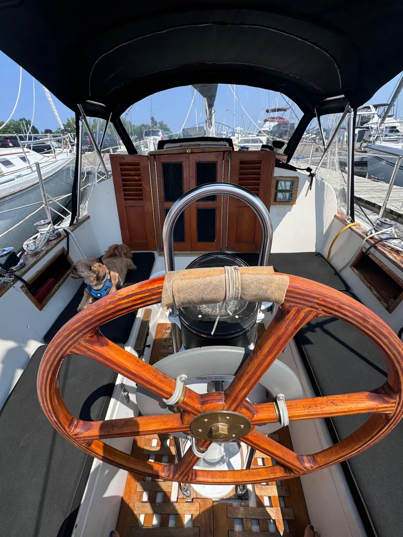 Slide: The Image of 1985 Bayfield 32 sailboat cockpit with wooden wheel and marina background. - 14