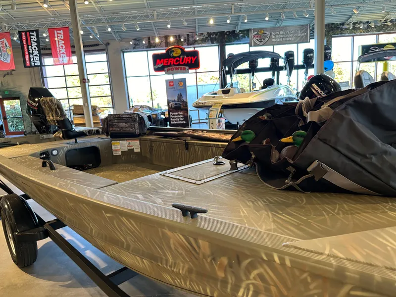 Slide: The Image of 2025 Tracker Grizzly 1654 T Sportsman boat displayed in a showroom with gear. - 3