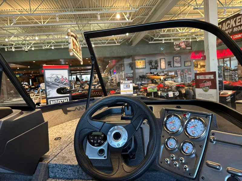 Slide: The Image of 2025 Tracker Pro Guide V-175 WT boat dashboard in showroom with steering wheel and gauges. - 2