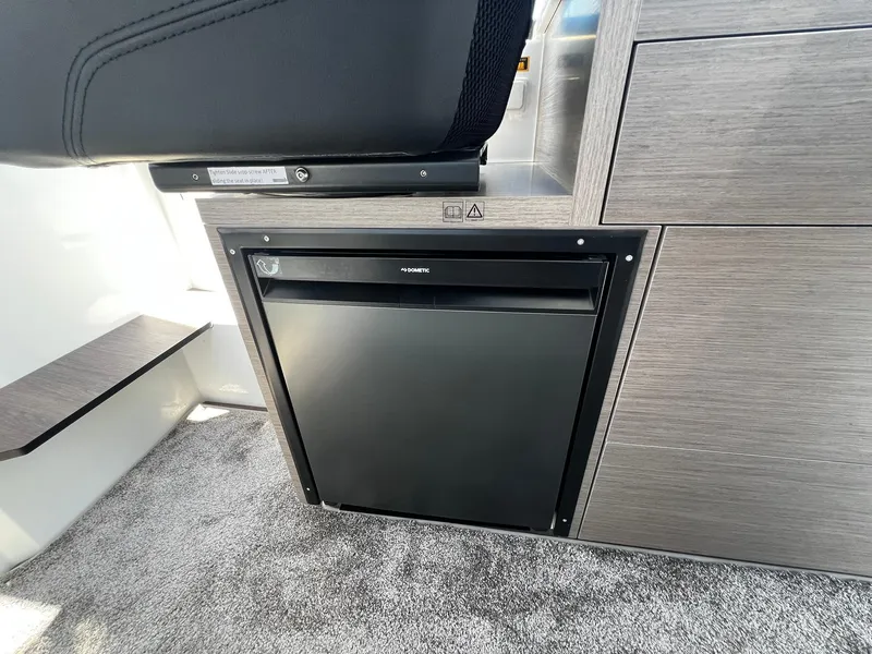 Slide: The Image of 2025 Jeanneau NC 895 interior with Dometic fridge, modern wood finish, and carpeted flooring. - 11