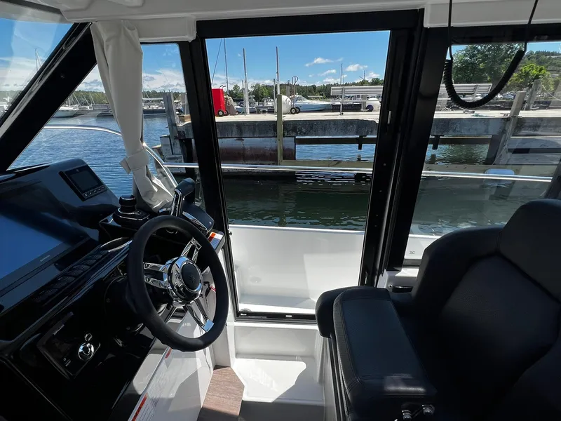 Slide: The Image of Interior view of 2025 Jeanneau NC 895 boat cockpit with steering wheel and waterfront background. - 13