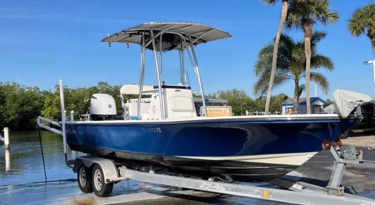 Slide: The Image of 2015 Sea Born FX24 Bay boat on trailer, blue hull, palm trees in background. - 2