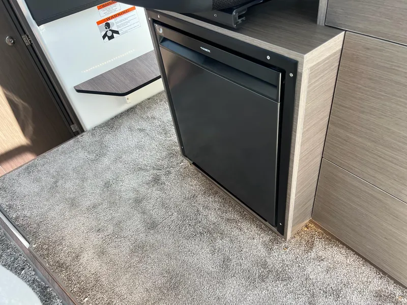 Slide: The Image of 2025 Jeanneau NC 895 Sport S2 interior with compact refrigerator and carpeted flooring. - 7