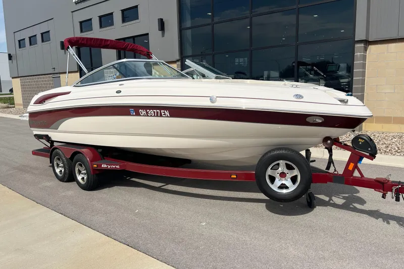 The Image of 2008 Bryant 239 boat on red trailer, parked near a modern building. - 1