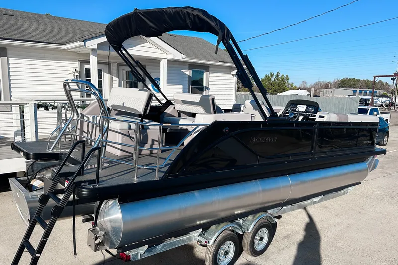 Slide: The Image of 2025 Godfrey Sweetwater 24' Drop Table Lounge Tritoon on trailer, black exterior, sunny day. - 25