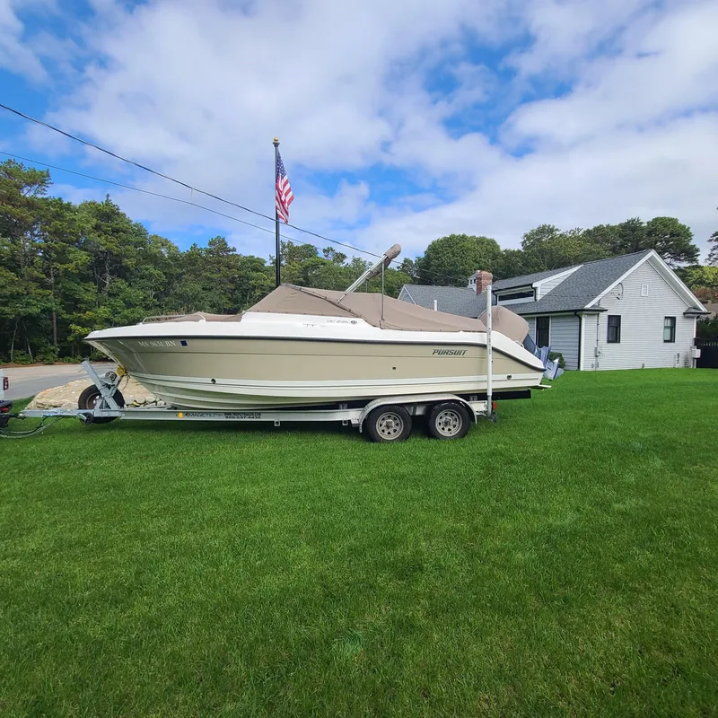 Slide: The Image of 2015 Pursuit DC 235 Dual Console boat on trailer, parked on grass near house. - 2