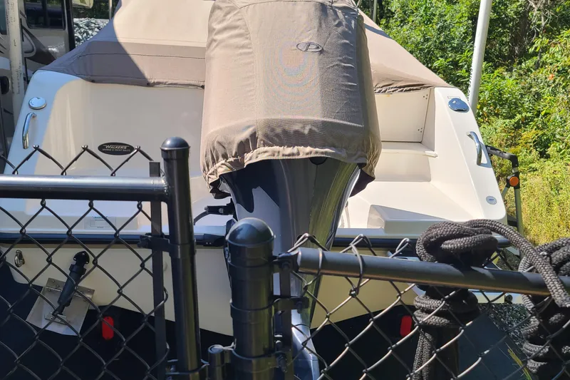 Slide: The Image of 2015 Pursuit DC 235 Dual Console boat behind a fence, covered engine, outdoor setting. - 24