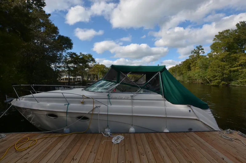 Slide: The Image of 1999 Rinker 270 Fiesta Vee boat docked on a serene lake with green canopy. - 0
