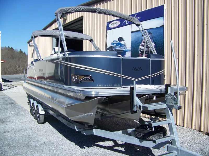 Slide: The Image of 2025 Avalon LSZ25QLS pontoon boat on trailer, parked outside a metal building. - 3