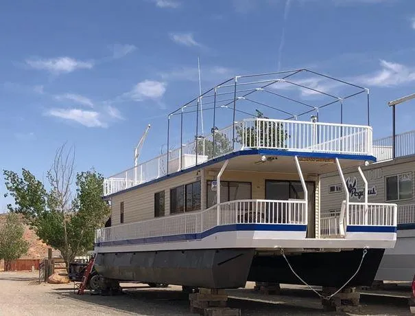 The Image of 1986 Hanson houseboat with upper deck, docked on land under a clear blue sky. - 0