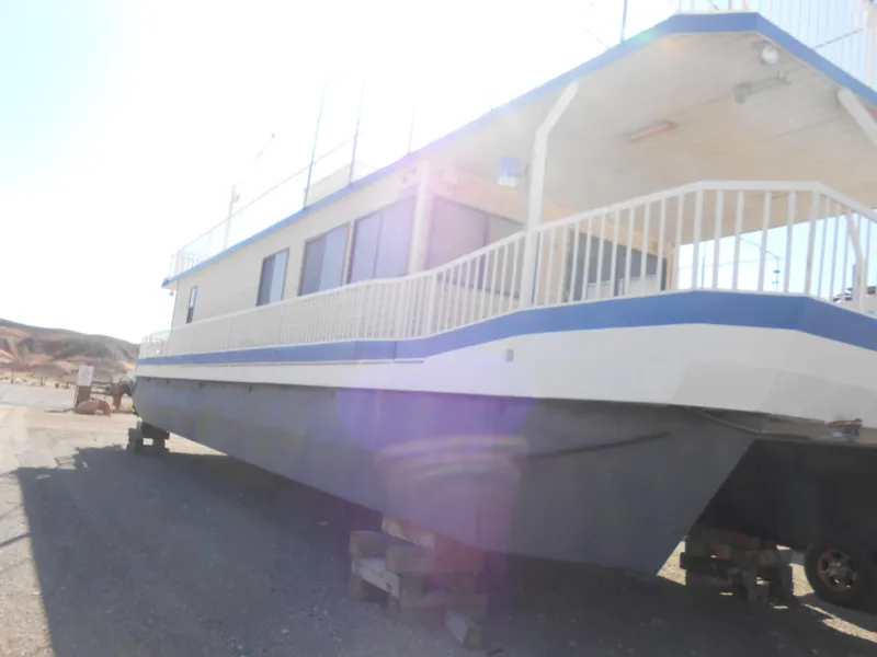 Slide: The Image of 1986 Hanson houseboat with blue trim, docked on land under bright sunlight. - 4