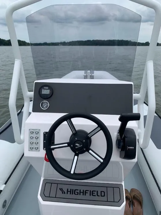 Slide: The Image of 2023 Highfield Patrol 540 boat dashboard with steering wheel on a calm lake. - 4