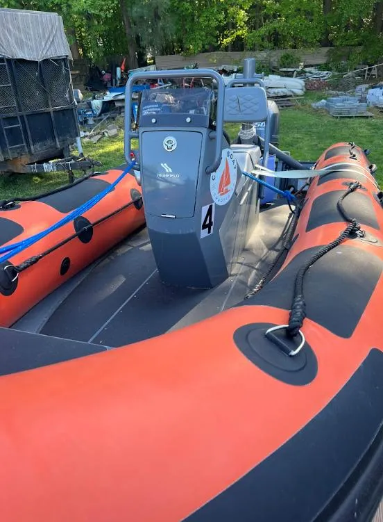 Slide: The Image of 2023 Highfield Patrol 460 inflatable boat with orange and black design, parked outdoors. - 1