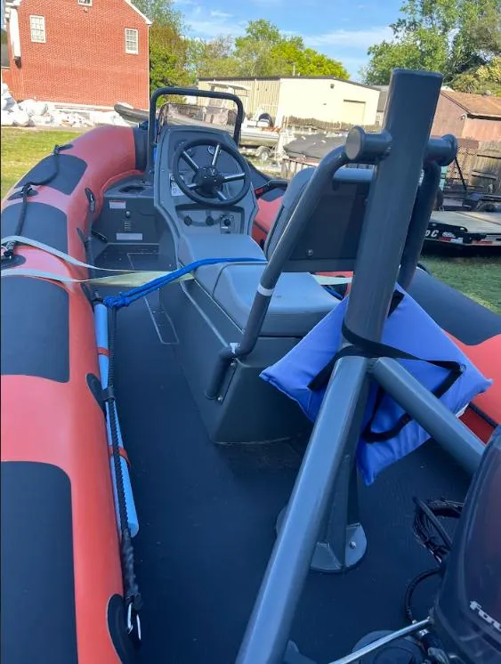 Slide: The Image of 2023 Highfield Patrol 460 boat with orange and black design, parked outdoors. - 2